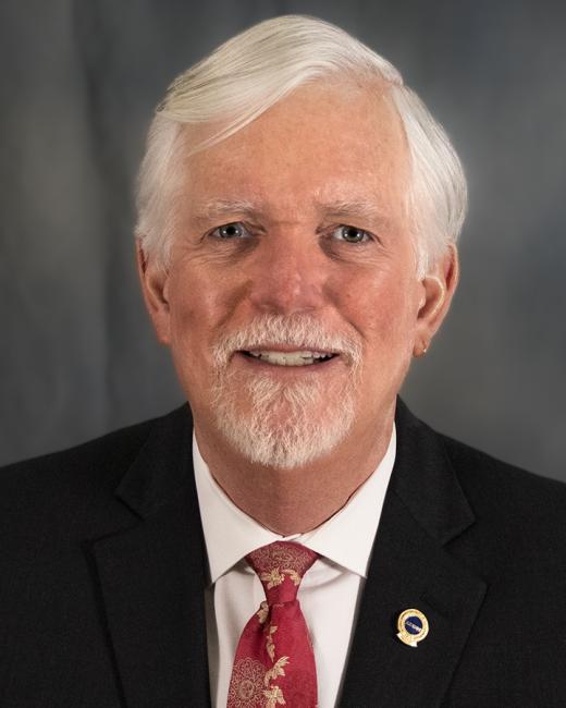 Photo of Roger Miller, a man wearing a red tie and a black suit.