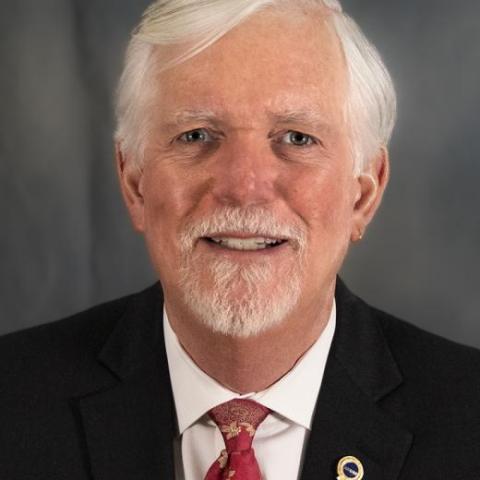 Photo of Roger Miller, a man wearing a red tie and a black suit.